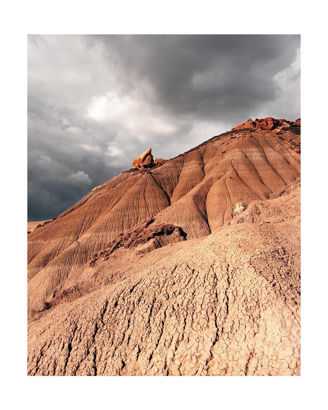 A barren, cracked hillside rises under a dramatic, cloudy sky.