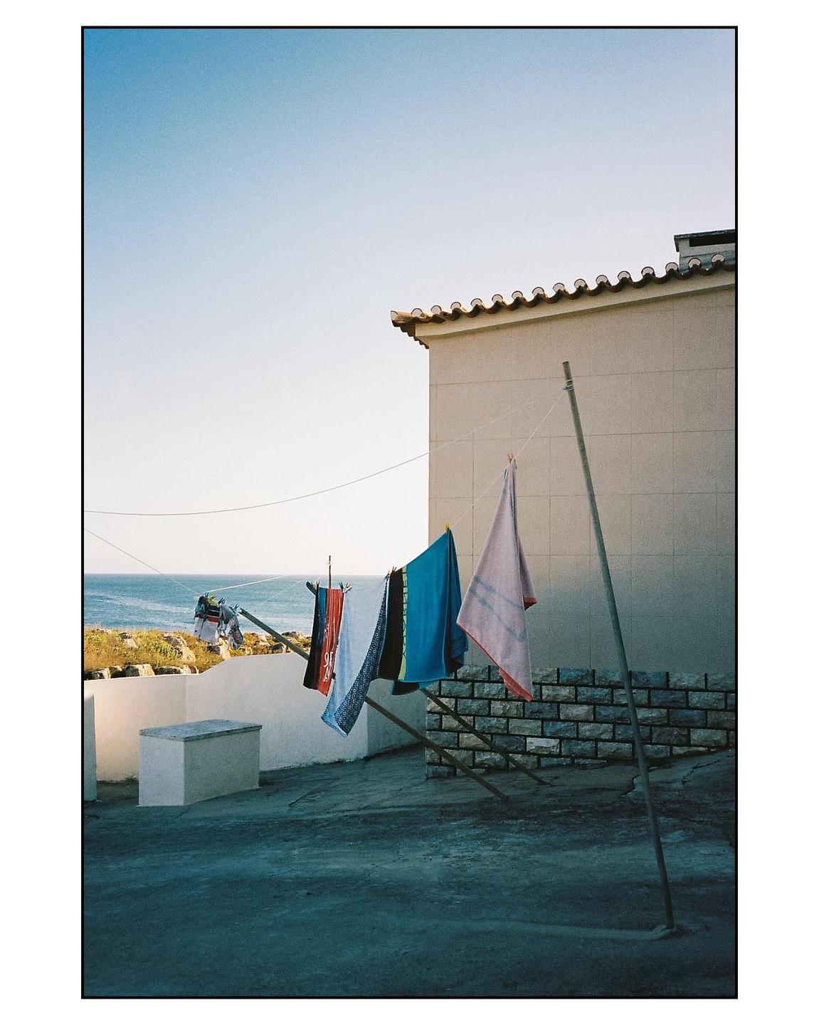 Clothes hang on a clothesline with a building and the ocean in the background.