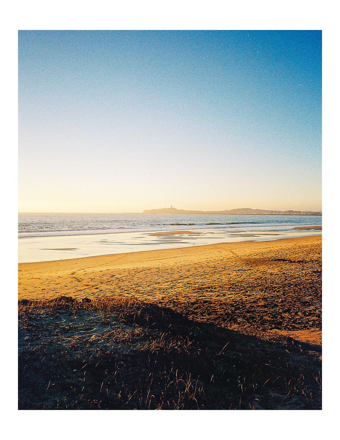 A sandy beach with gentle waves under a clear sky during golden hour.