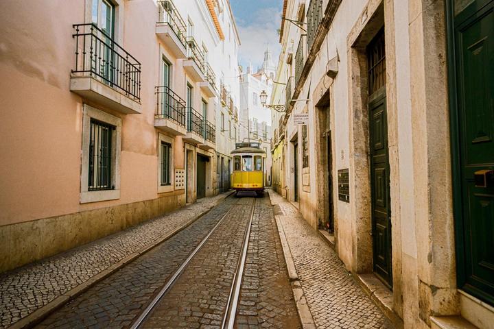 A yellow tram travels down a narrow cobblestone street lined with buildings in Lisbon.