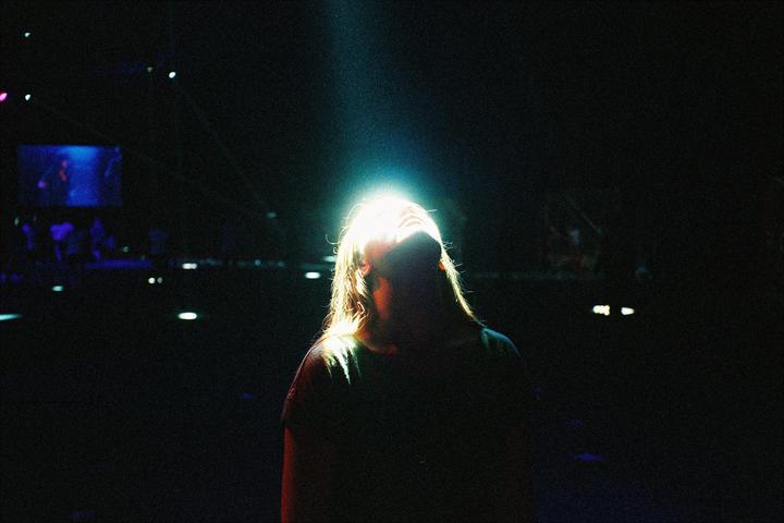 A woman with long hair is illuminated by a bright light from above, with her head tilted back.