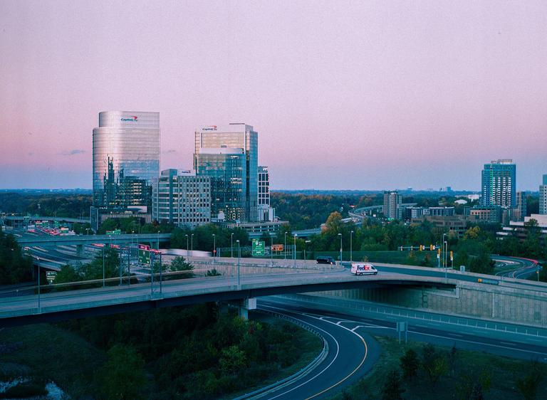 A cityscape with multiple buildings and highways is visible under a pink and purple sky at dusk.