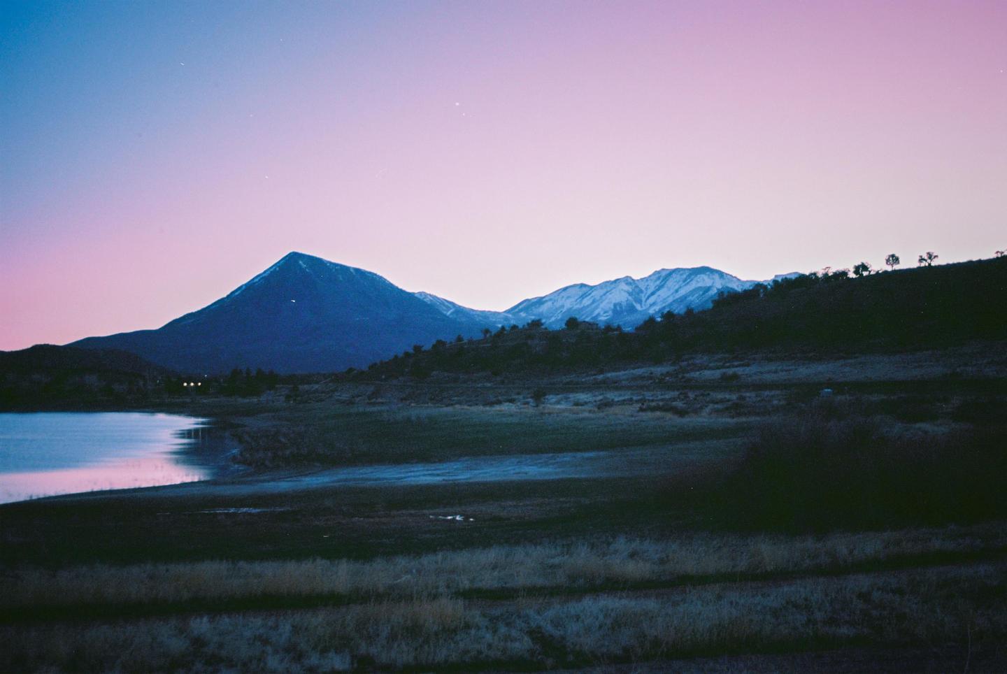 A lake reflects the pink and blue sky at dusk, with mountains and hills in the background.