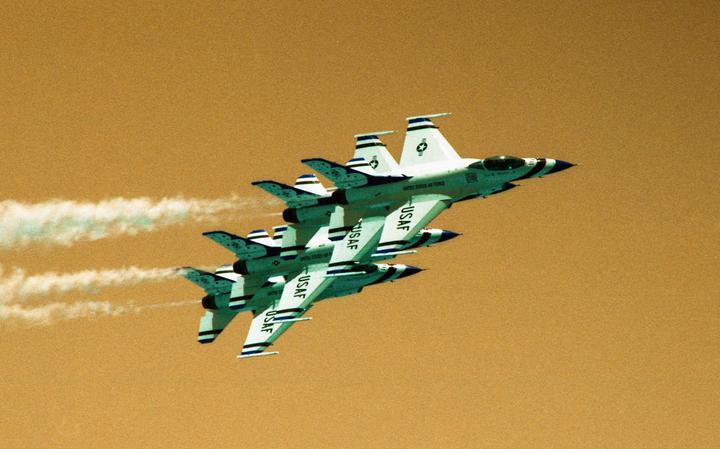 Four fighter jets fly in formation against an orange sky, leaving white contrails.