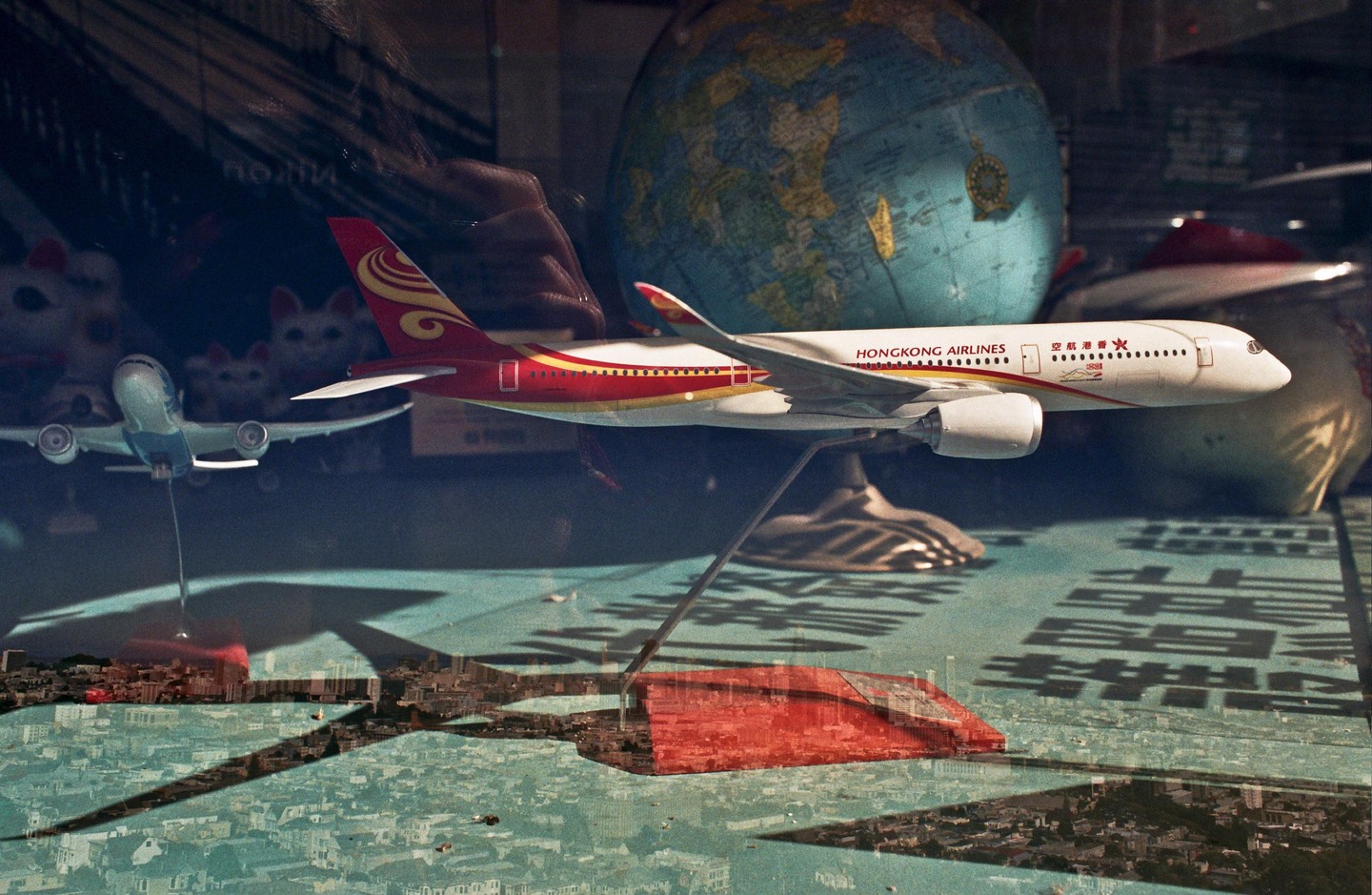 A model airplane is displayed in a window with a double exposure of a city.
