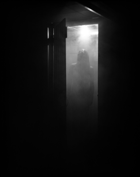 A woman stands in a doorway, illuminated by bright light and surrounded by smoke.