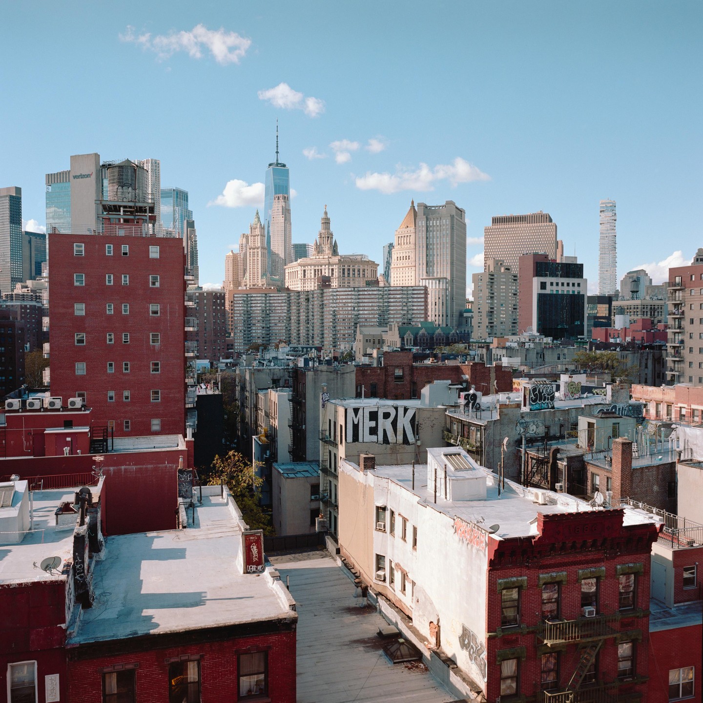 A panoramic view of Lower Manhattan shows a mix of old and new buildings under a clear sky with scattered clouds.