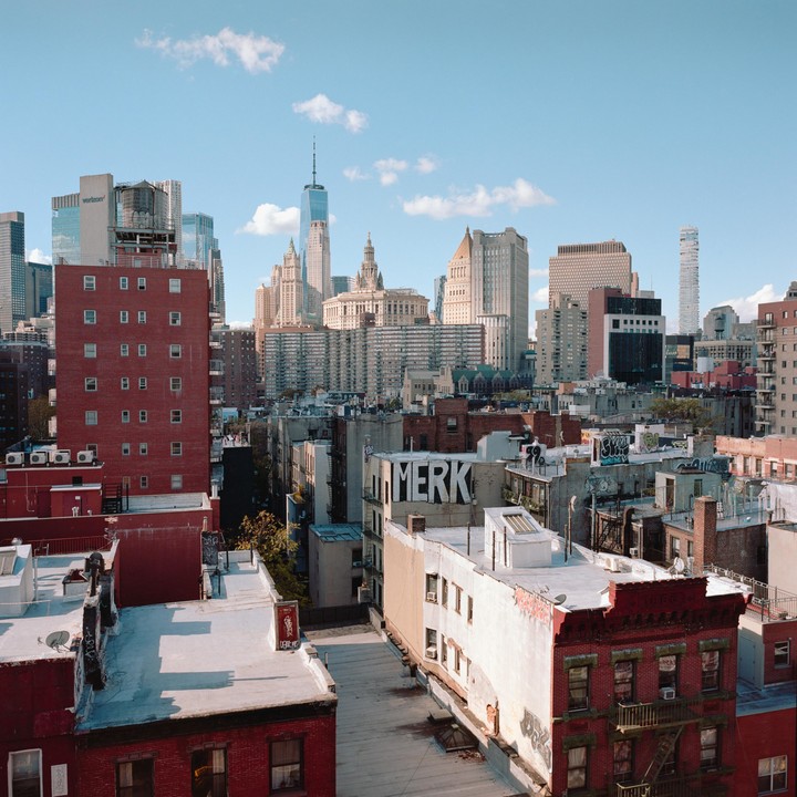 A panoramic view of Lower Manhattan shows a mix of old and new buildings under a clear sky with scattered clouds.