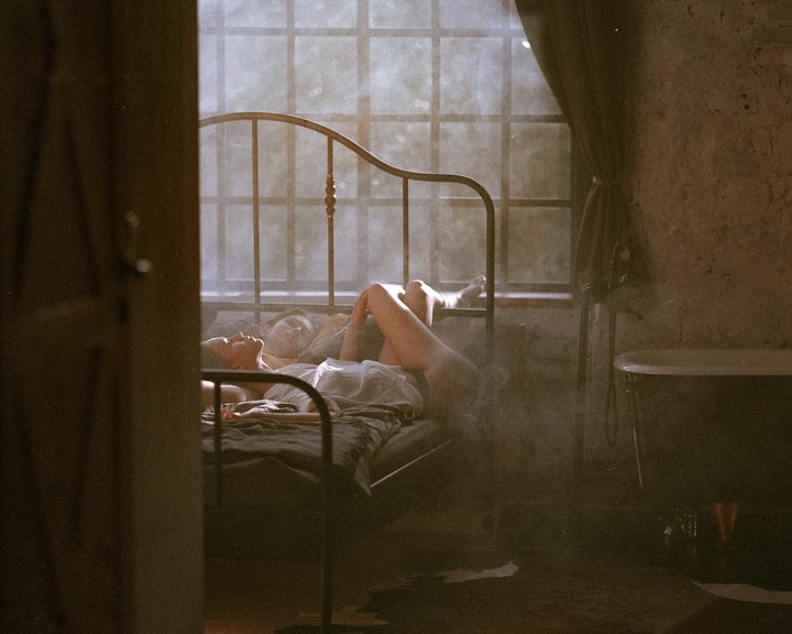 A woman lies on a bed in a hazy room with a window and a bathtub.