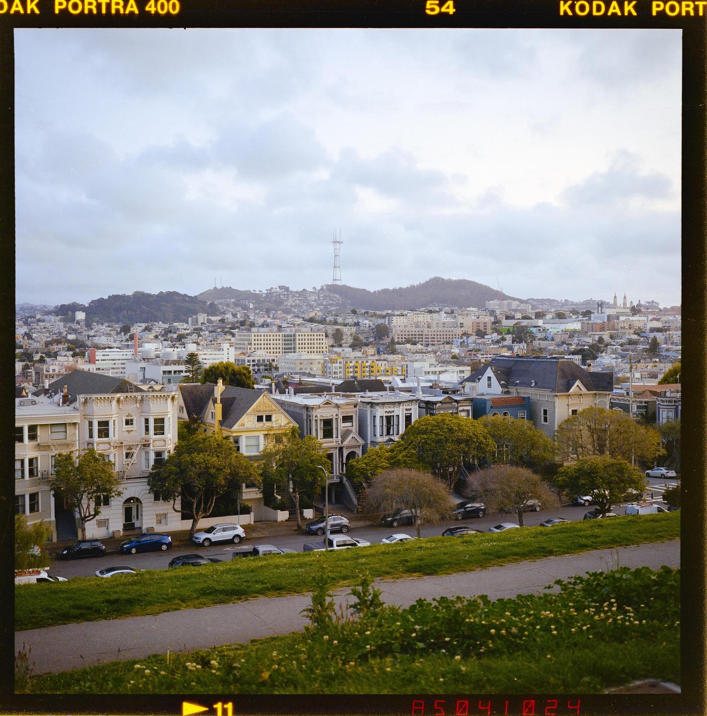 A city skyline with a prominent tower on a hill is visible beyond a row of houses and a grassy slope.