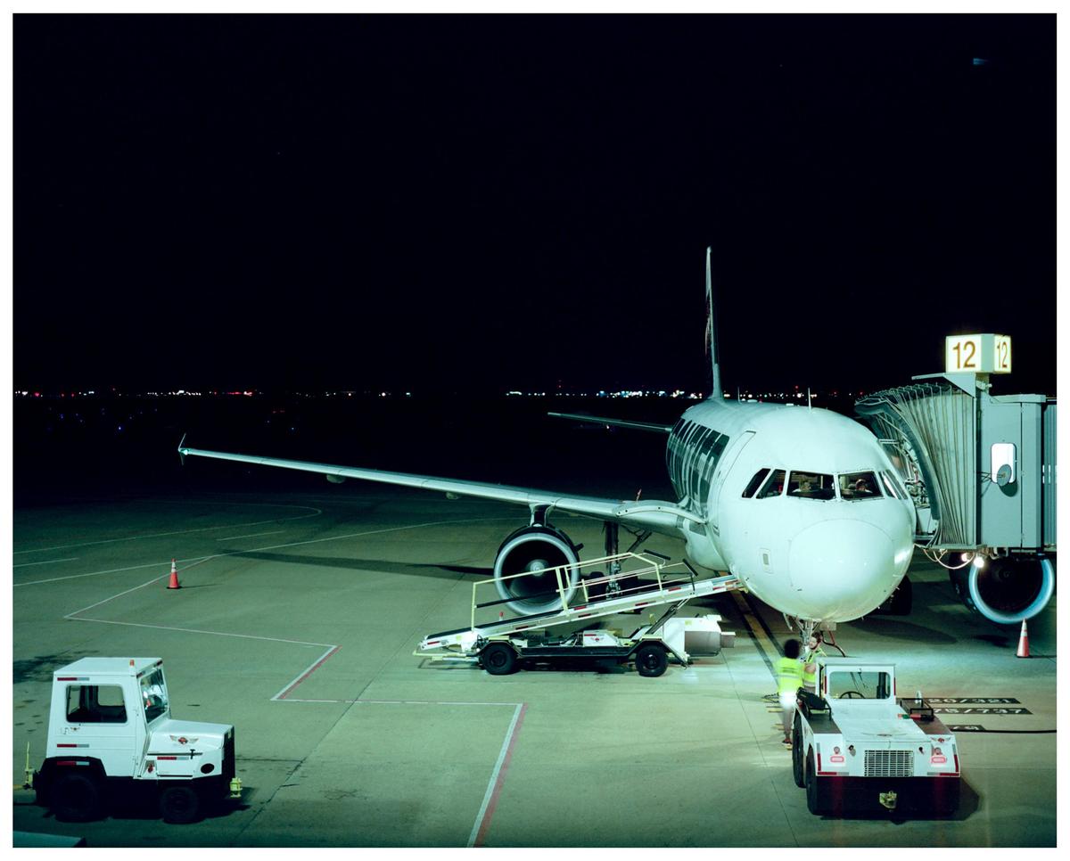 An airplane is parked at a gate on an airport tarmac at night, with ground crew vehicles nearby.