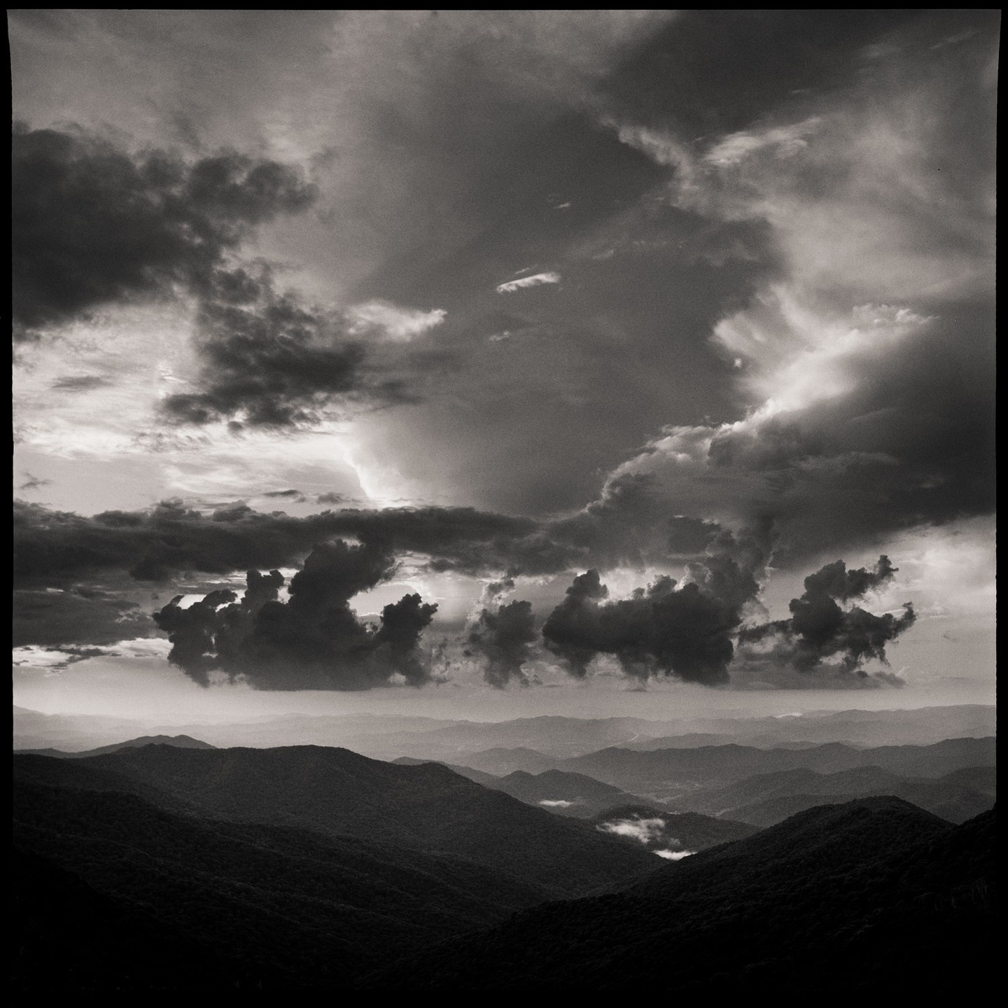Dark clouds hang over a mountain range with a valley visible in the distance.