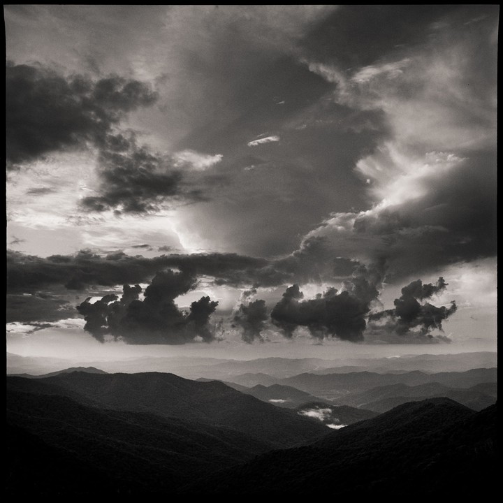 Dark clouds hang over a mountain range with a valley visible in the distance.