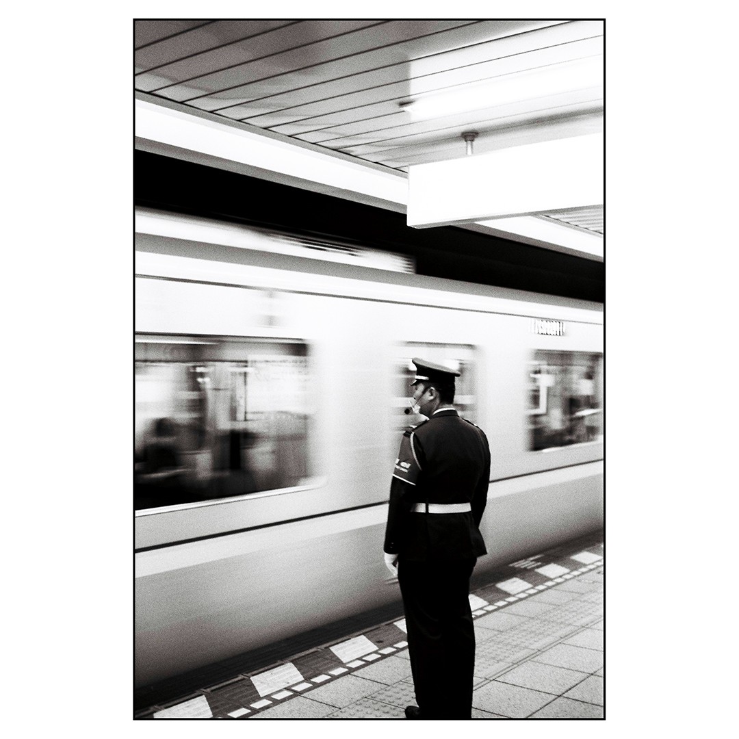 A man in uniform stands on a subway platform as a train passes by.