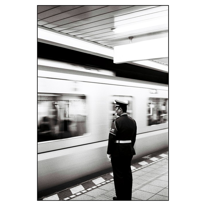 A man in uniform stands on a subway platform as a train passes by.