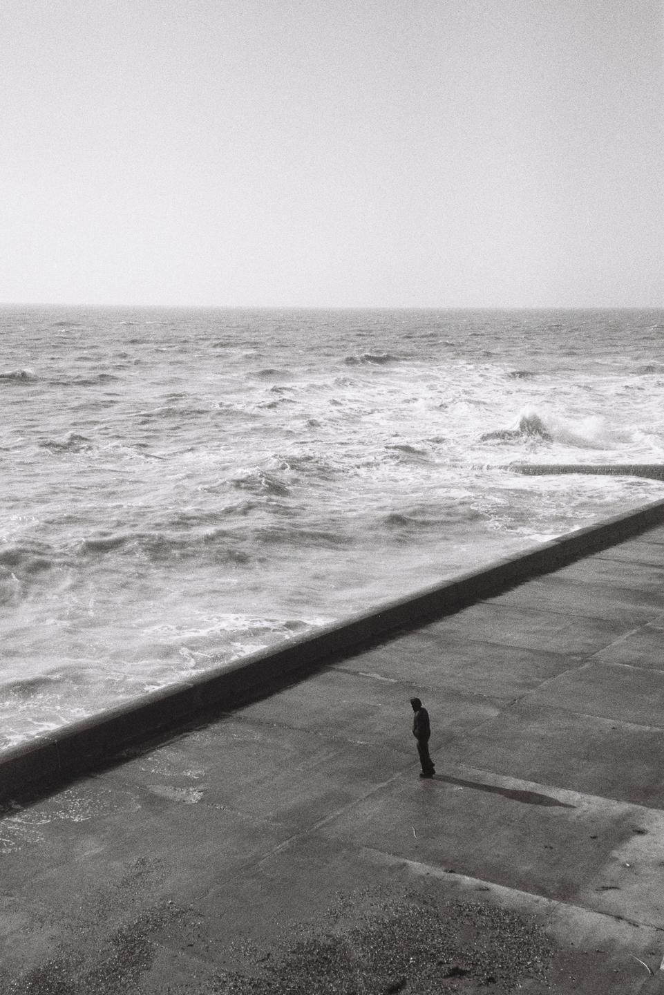 A man stands on a concrete pier looking out at the ocean.