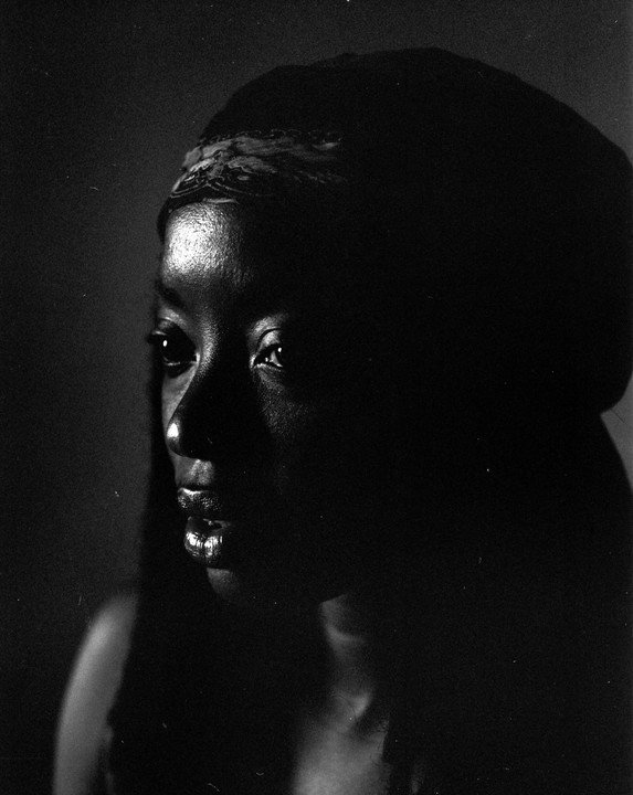 A woman with a patterned headband is illuminated by light on the left side of her face.