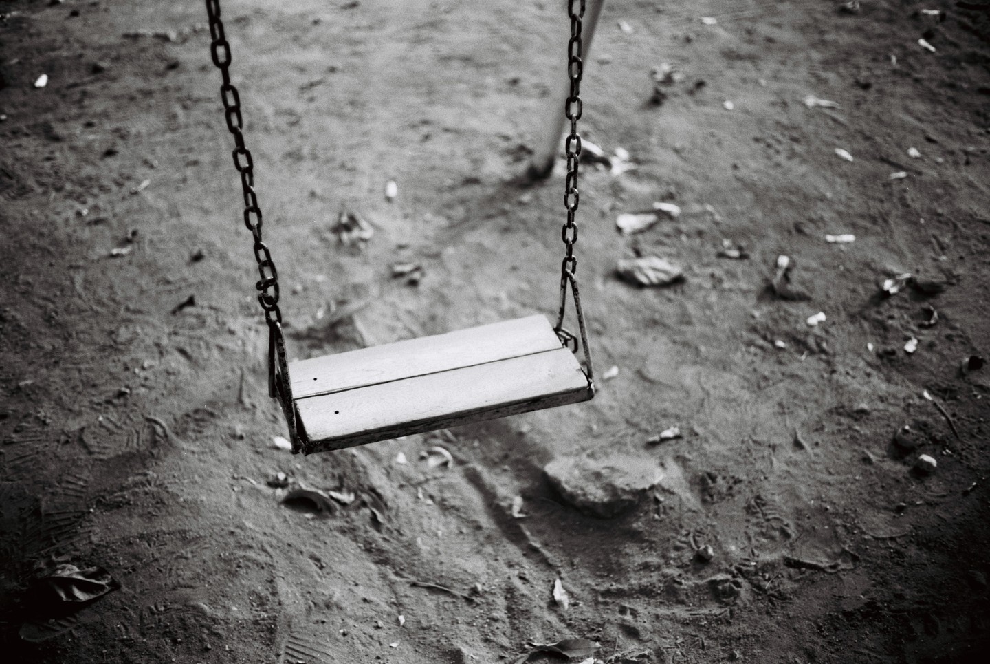 A wooden swing hangs over sandy ground with scattered debris.