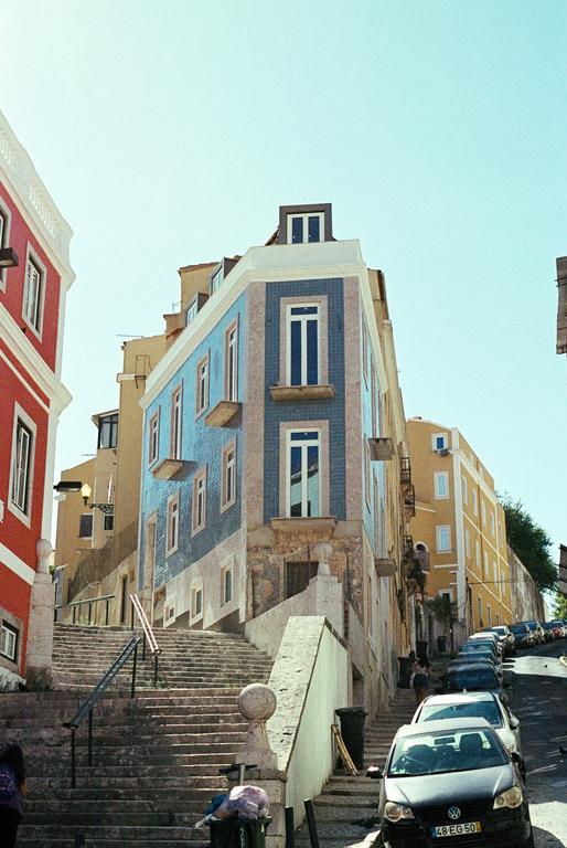 A blue and white tiled building stands at the corner of a street with parked cars and a long stone staircase.