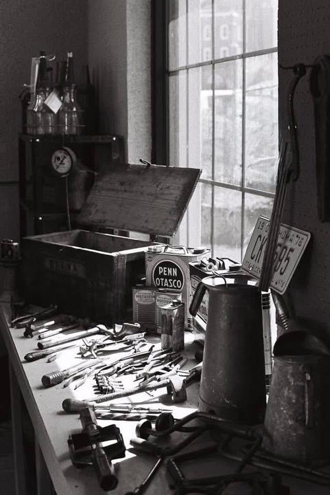 A collection of tools and containers are arranged on a workbench next to a window.