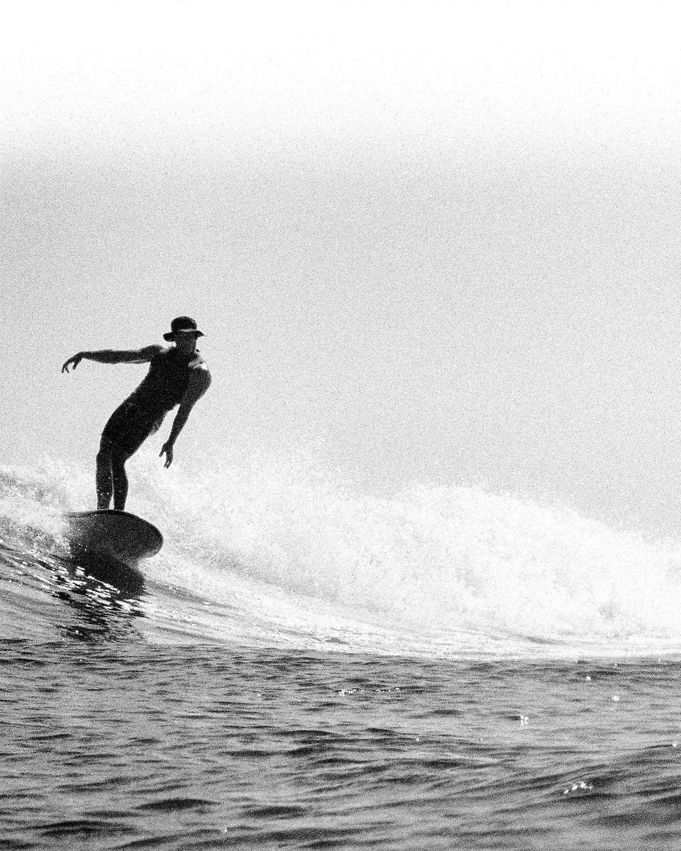 A surfer wearing a hat rides a wave.