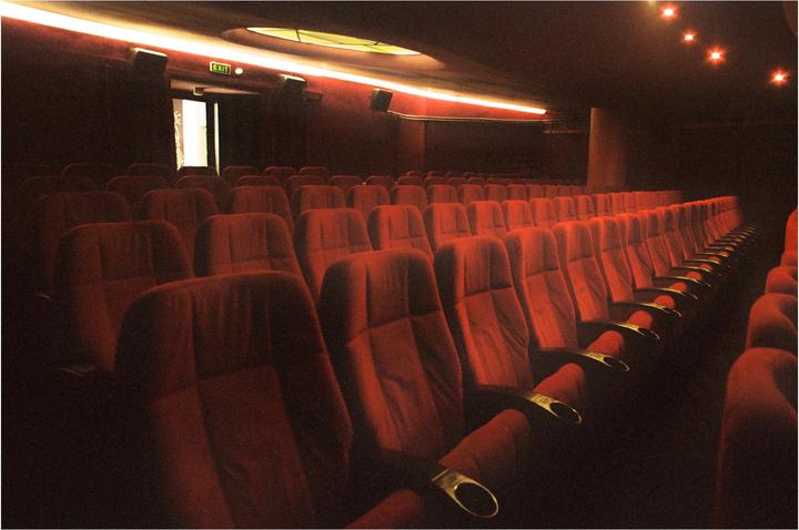An empty movie theater with rows of red seats and an exit sign above a doorway.