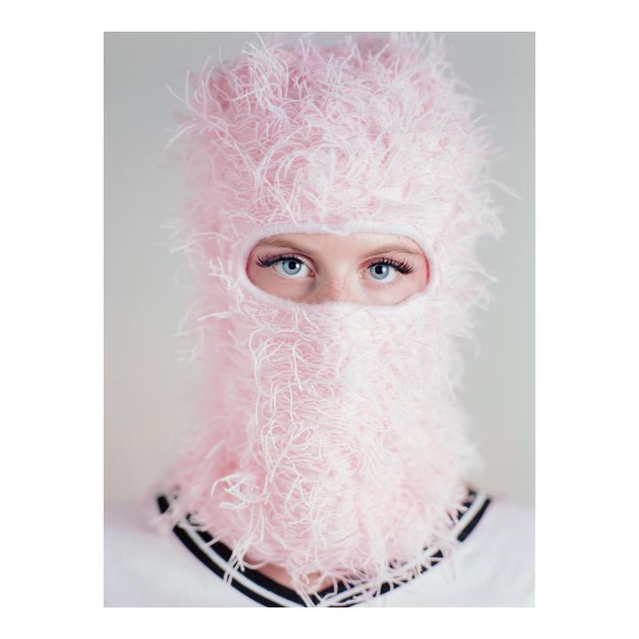 A woman with blue eyes looks directly at the viewer while wearing a pink balaclava.