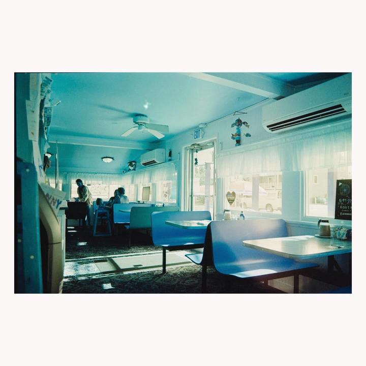 Sunlight streams into a diner with blue booths and a man standing near a counter.
