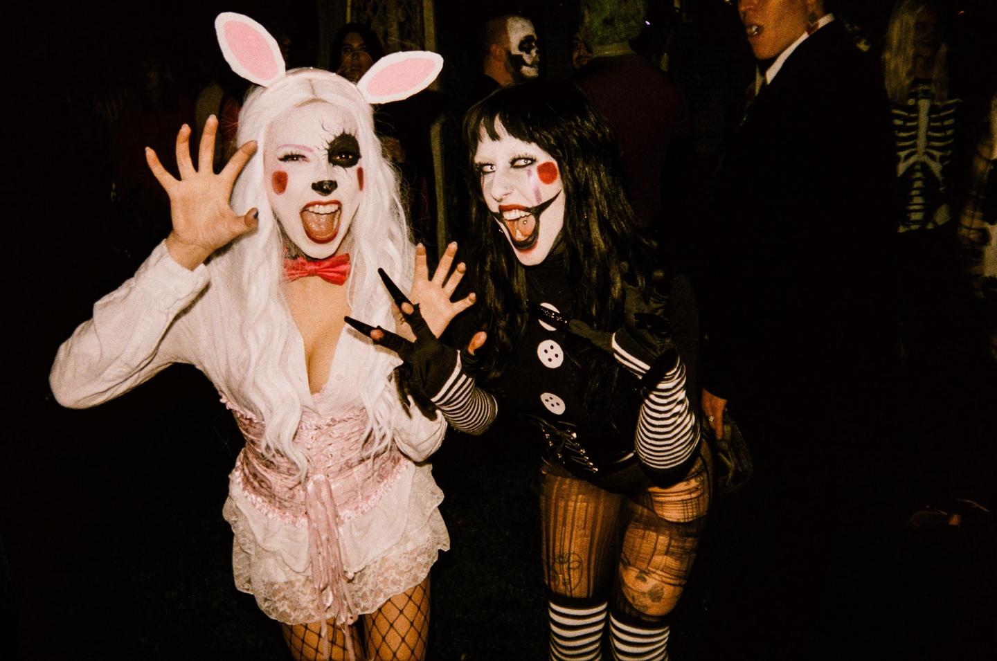 Two women in elaborate costumes and makeup pose for the camera at night.
