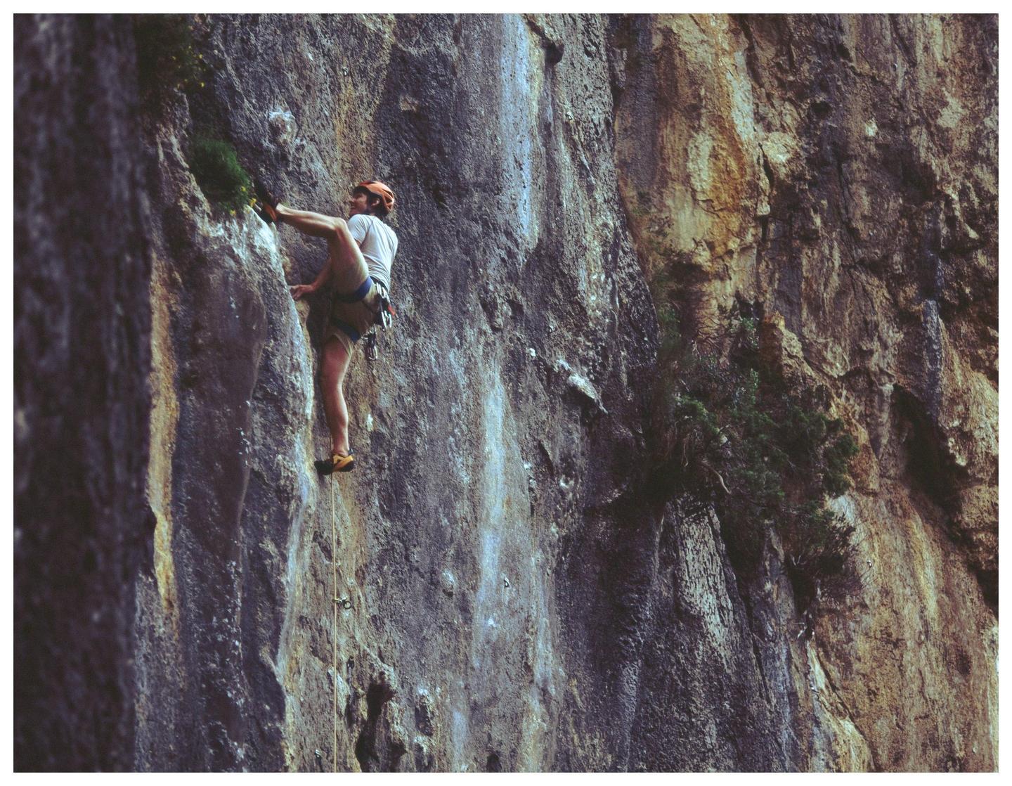 A man in a helmet and harness climbs a rock face.
