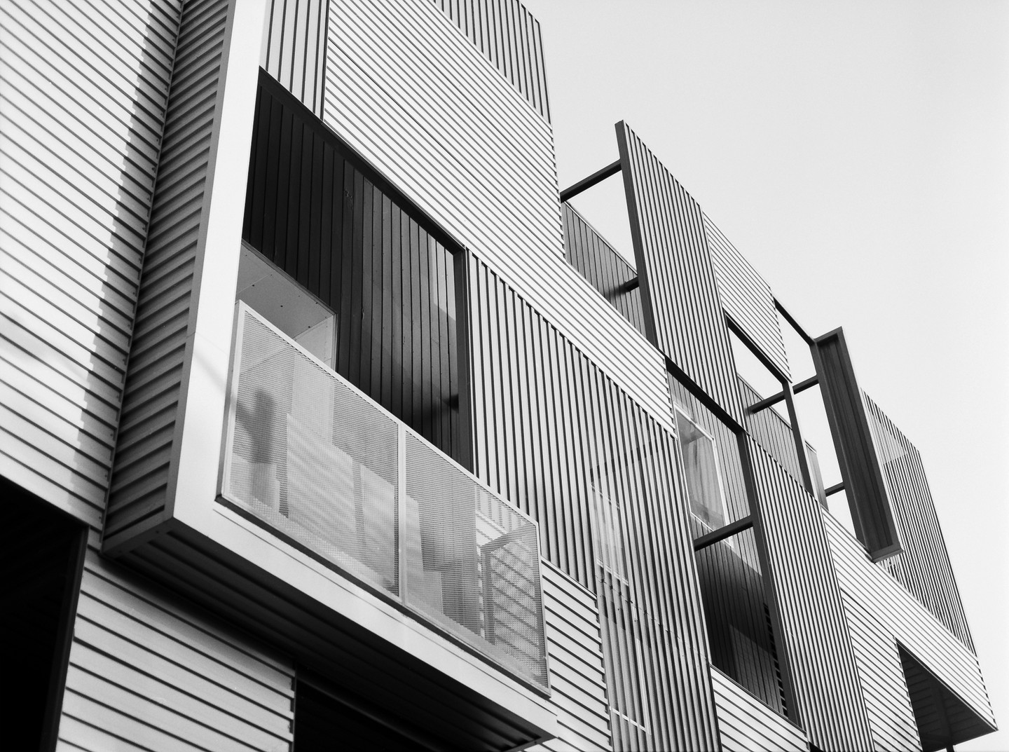 A modern building with horizontal and vertical siding features a balcony with a mesh railing.
