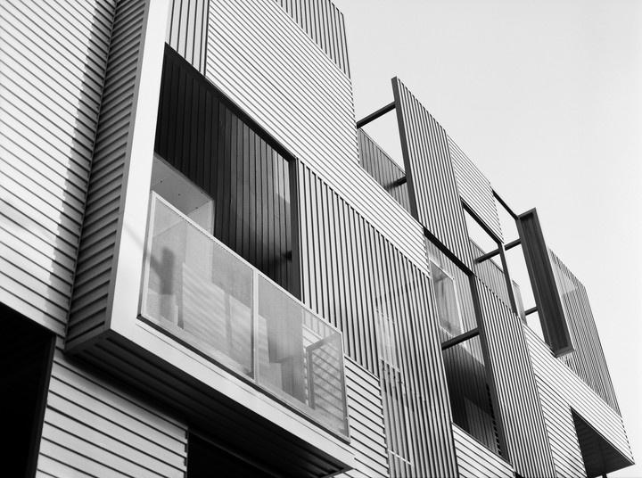 A modern building with horizontal and vertical siding features a balcony with a mesh railing.