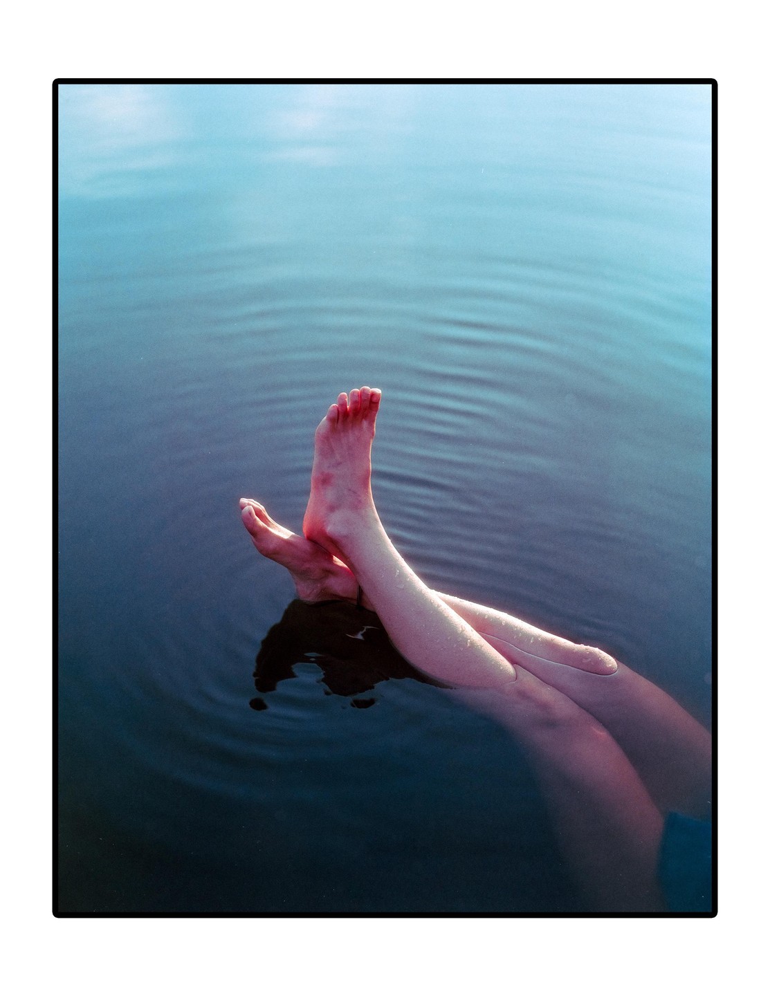 A person's legs and feet are submerged in blue water, creating ripples on the surface.
