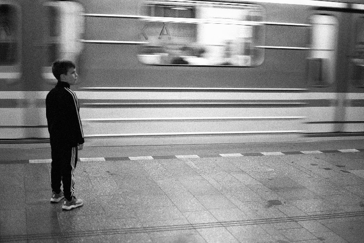 A boy stands on a subway platform as a train passes by.