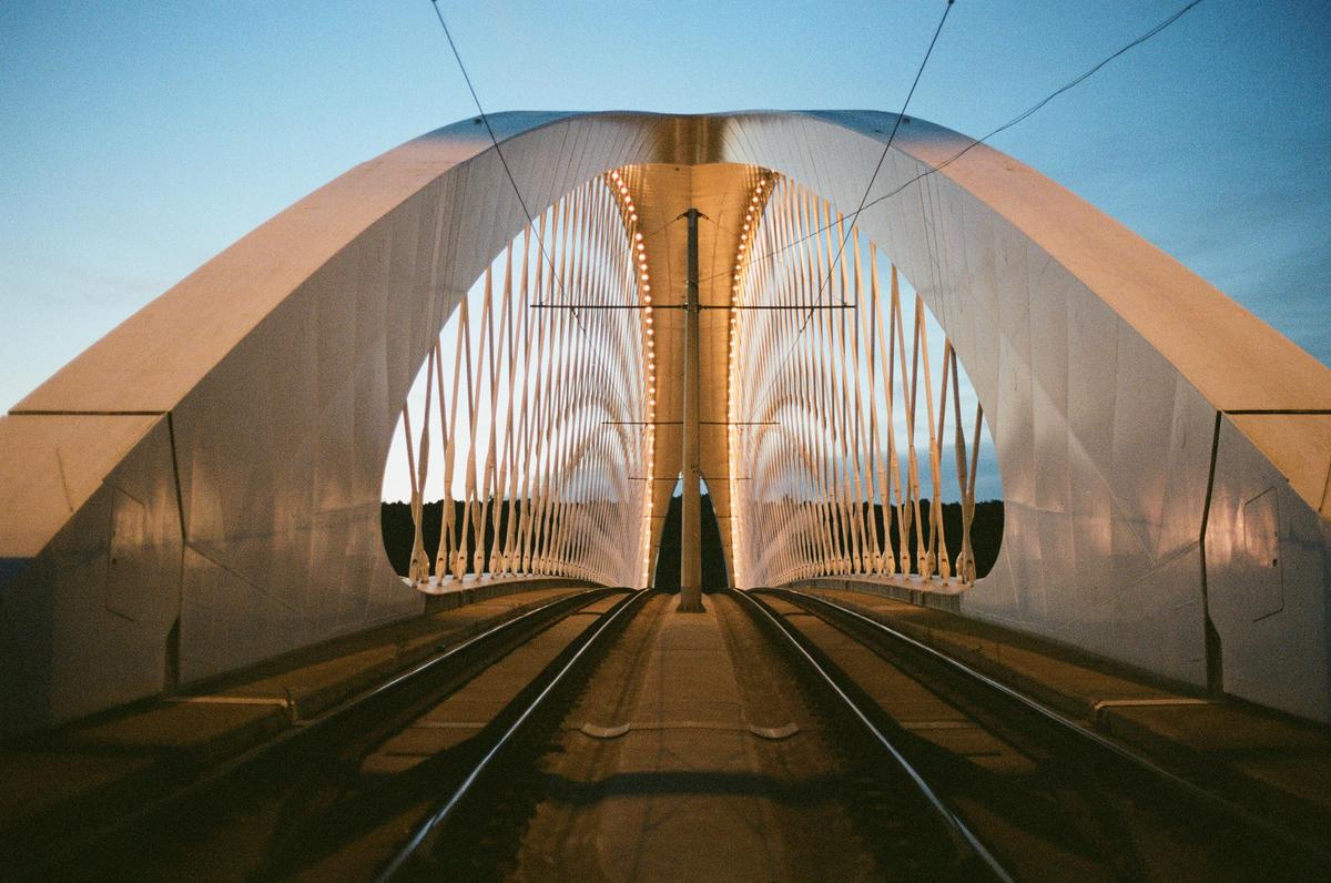 A tram bridge with illuminated arches stretches into the distance under a clear sky.