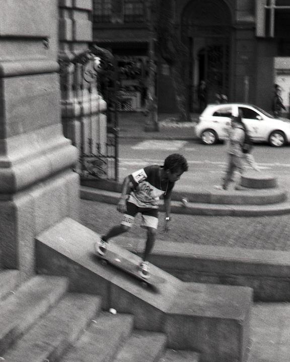 A boy on a skateboard rides down a concrete ramp on a city street.
