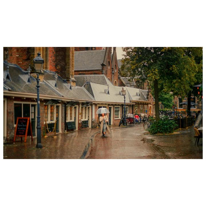 A woman with an umbrella walks down a wet street lined with brick buildings and bicycles.