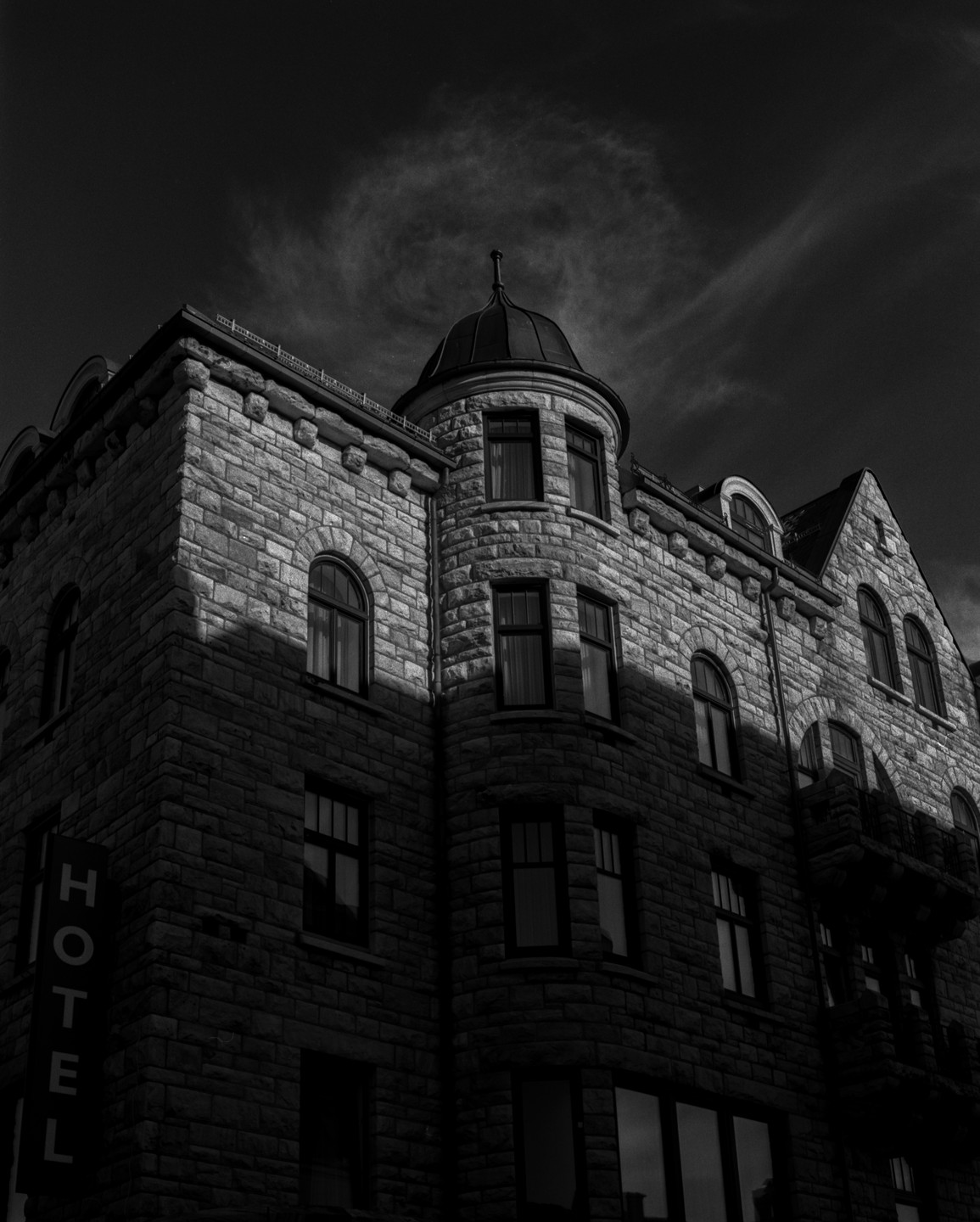 A stone hotel building with a turret is partially illuminated by sunlight under a dark sky.