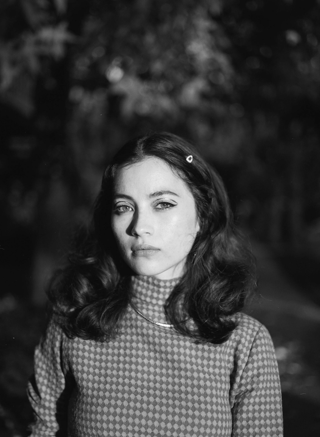 A woman with long, wavy hair and a patterned turtleneck sweater looks directly at the viewer.