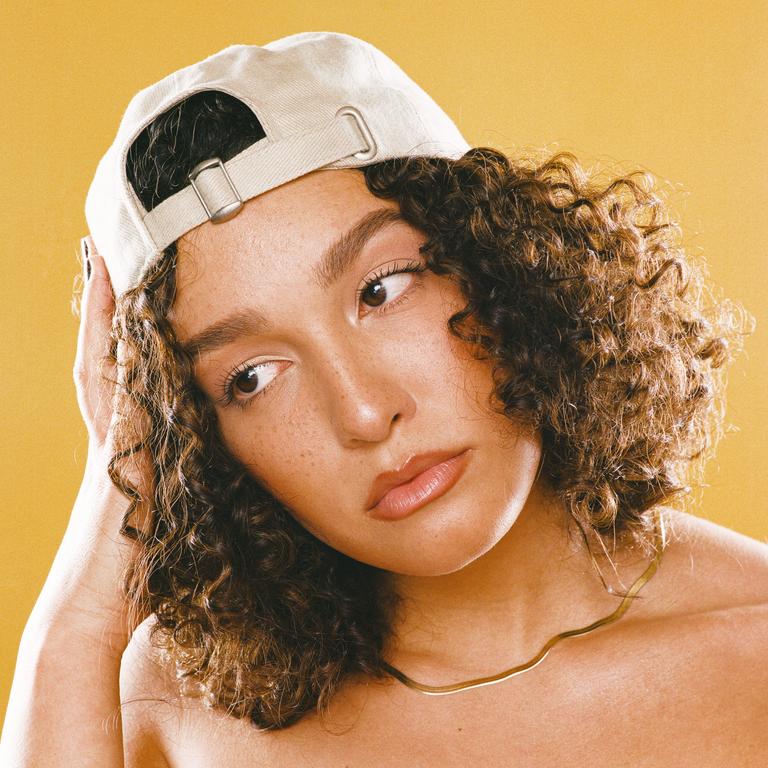 A woman with curly hair and a baseball cap looks to the side.
