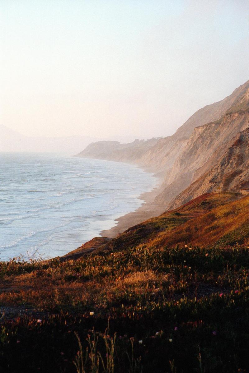 A hazy coastline with cliffs and a beach is visible under a bright sky.