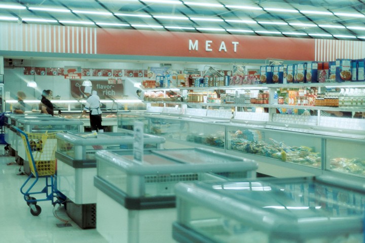 A grocery store meat department with a chef behind the counter and several freezer cases in the foreground.