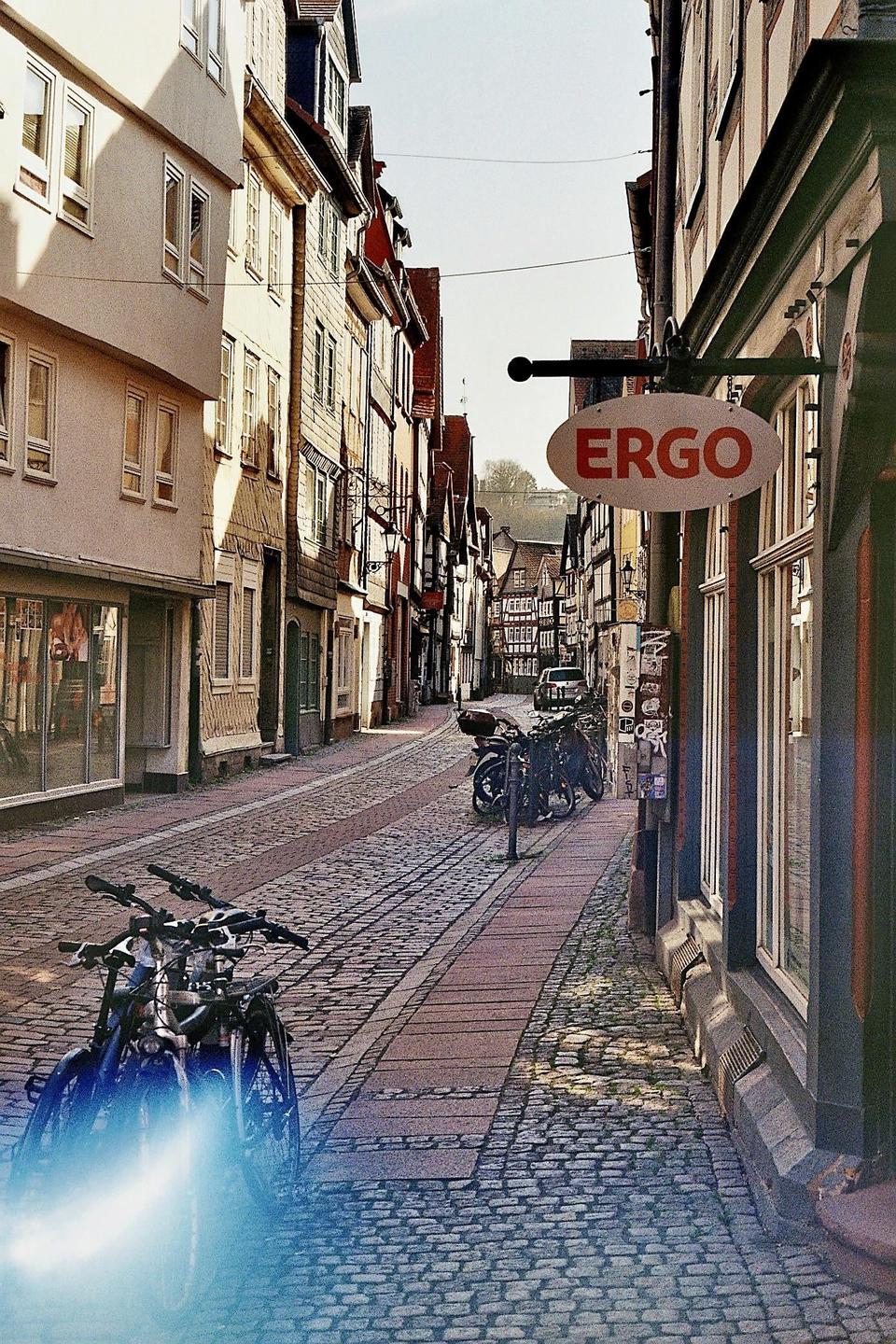 A narrow cobblestone street is lined with buildings and parked bicycles under a bright sky.