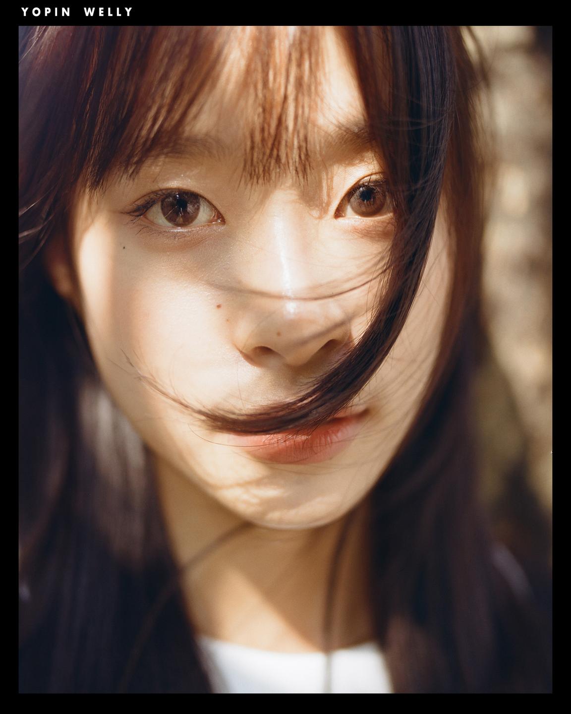 A girl with long hair looks directly at the viewer, with sunlight casting shadows on her face.