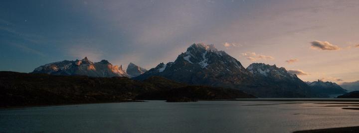A wide shot shows a lake with mountains in the background under a starry sky.