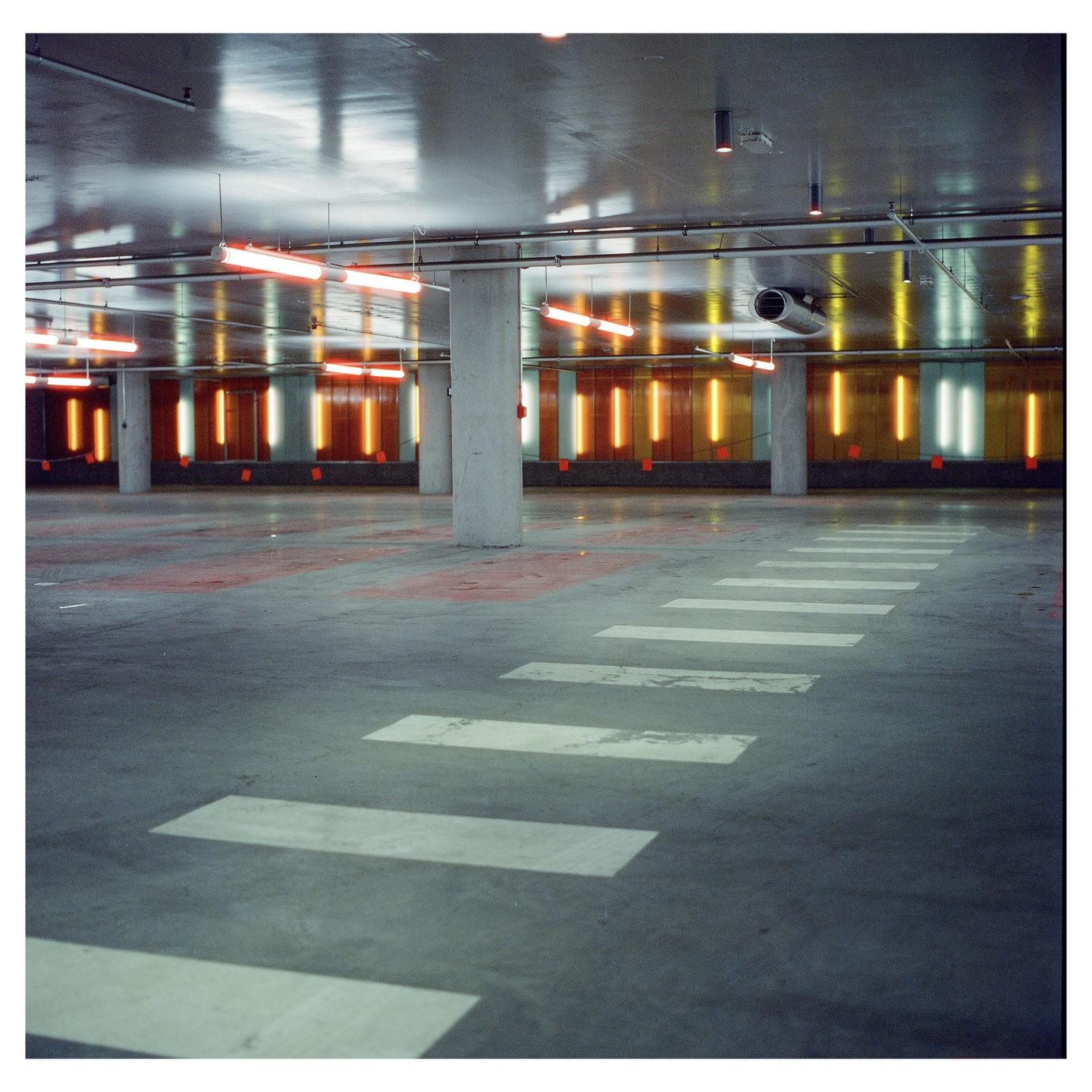 An empty parking garage is illuminated by orange and white neon lights.