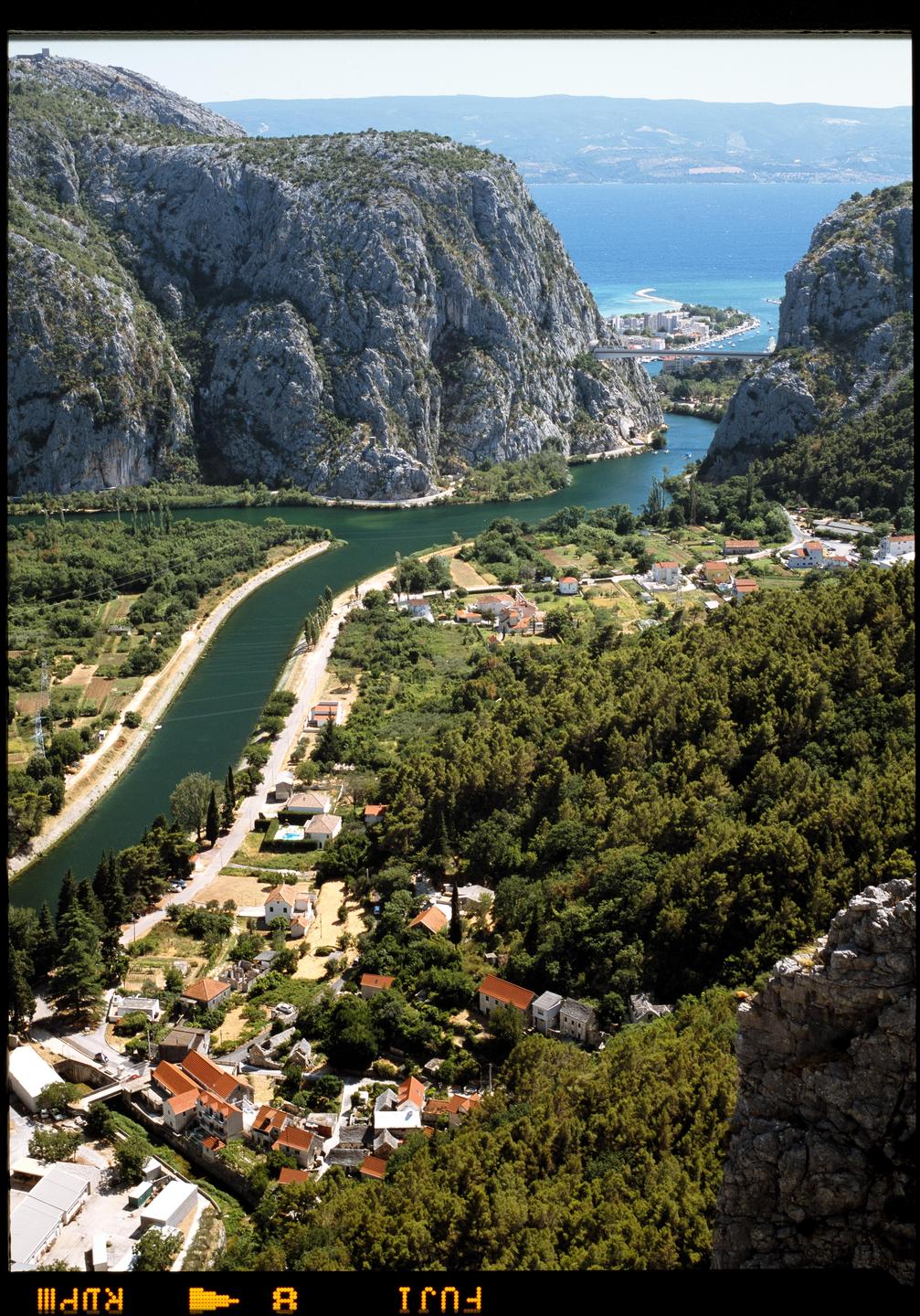 A river winds through a valley with a town nestled between mountains and the sea.