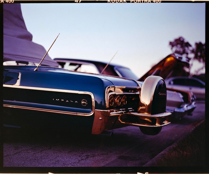A dark blue 1964 Chevrolet Impala is parked on a street with its trunk open.