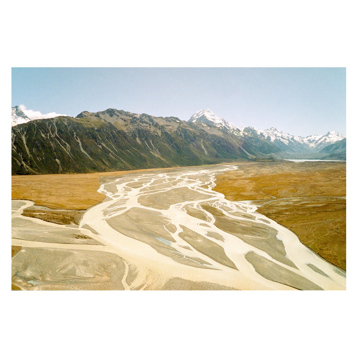 A wide river with many braided channels flows through a valley with mountains in the background.