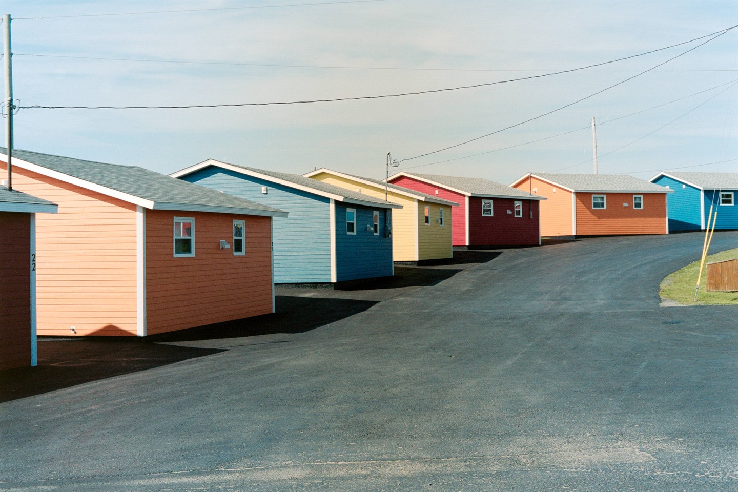 A row of colorful houses with white trim lines a paved road under a clear sky.